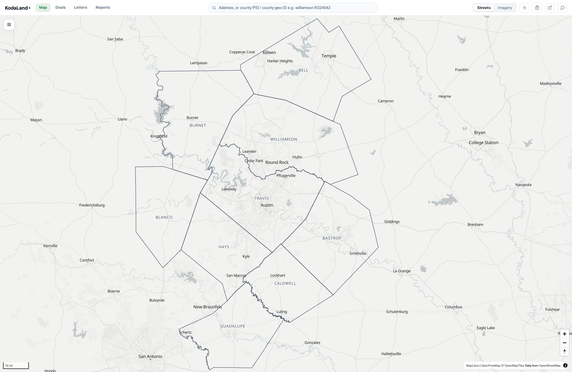 The KodaLand map zoomed all the way out to the whole nine-county Austin metro on the streets basemap, with the county boundaries drawn as clear slate lines and each county labeled: Bell, Burnet, Williamson, Travis, Blanco, Hays, Caldwell, Bastrop and Guadalupe. City labels sit throughout the metro (Georgetown, Round Rock, Austin, Leander, San Marcos, Killeen, Temple, New Braunfels), and the app's search bar reads 'Address, or county:PID / county:geo-ID'.